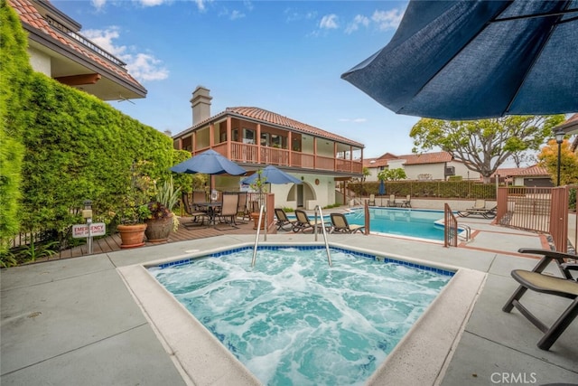 community pool with outdoor dining area, fence, a community hot tub, and a patio area