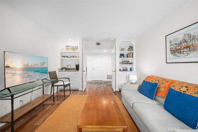 living room with wood finished floors, visible vents, and crown molding