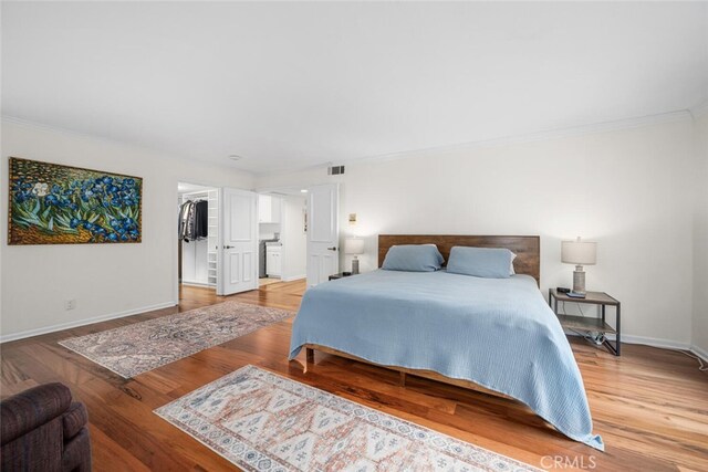 bedroom with light wood finished floors, visible vents, a walk in closet, crown molding, and baseboards