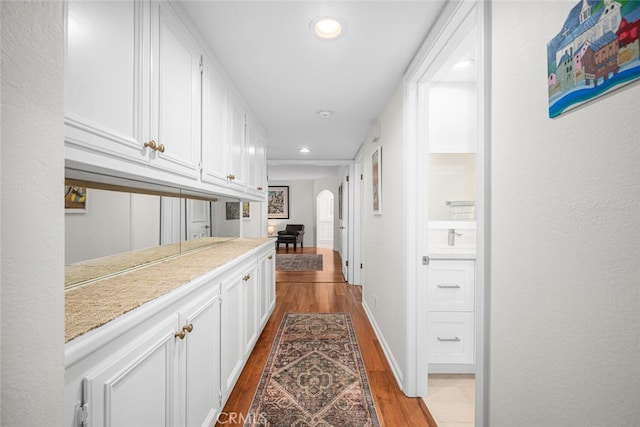 hallway featuring arched walkways, wood finished floors, and recessed lighting