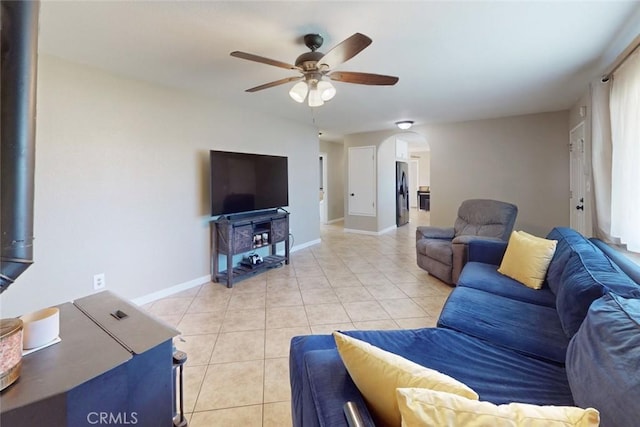 living room featuring baseboards, arched walkways, a ceiling fan, and light tile patterned floors
