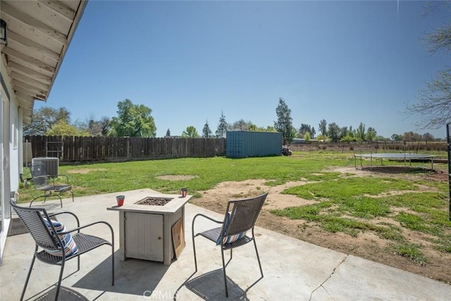 view of patio featuring cooling unit, a trampoline, a fenced backyard, and an outdoor fire pit