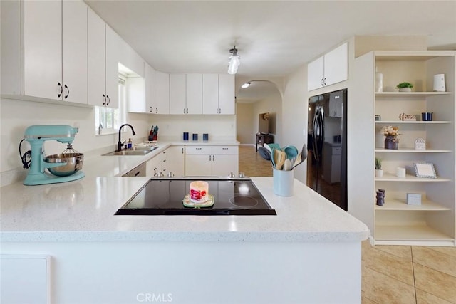 kitchen featuring a sink, black appliances, light tile patterned floors, arched walkways, and a peninsula