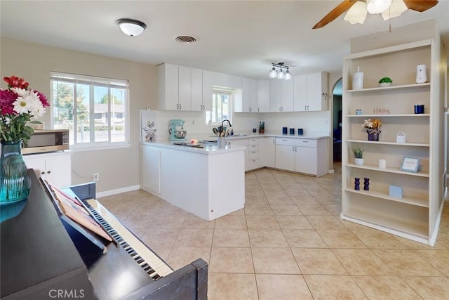 kitchen with light countertops, light tile patterned floors, stainless steel microwave, a sink, and a peninsula