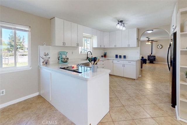 kitchen with a peninsula, black appliances, ceiling fan, light countertops, and light tile patterned floors