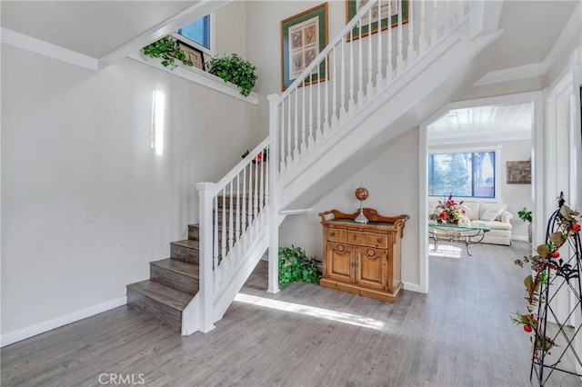 stairway featuring wood finished floors, a towering ceiling, and baseboards