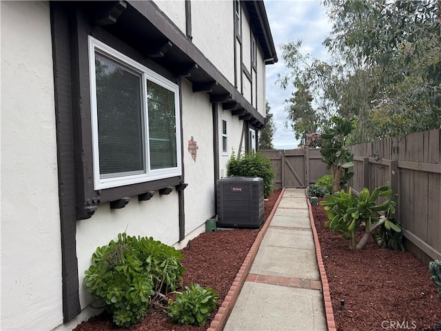 view of side of home with fence, central AC unit, a gate, and stucco siding