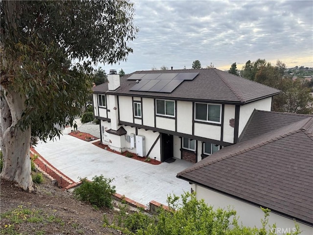 rear view of house with a chimney, solar panels, roof with shingles, and stucco siding