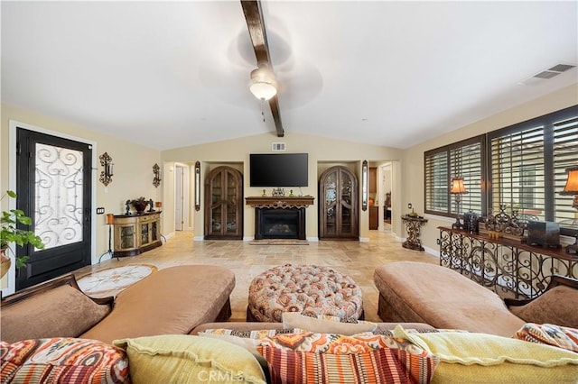 living area with a fireplace with flush hearth, visible vents, vaulted ceiling with beams, baseboards, and ceiling fan