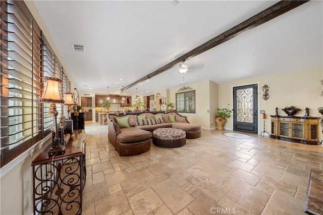 living area with baseboards, stone tile floors, beam ceiling, and visible vents