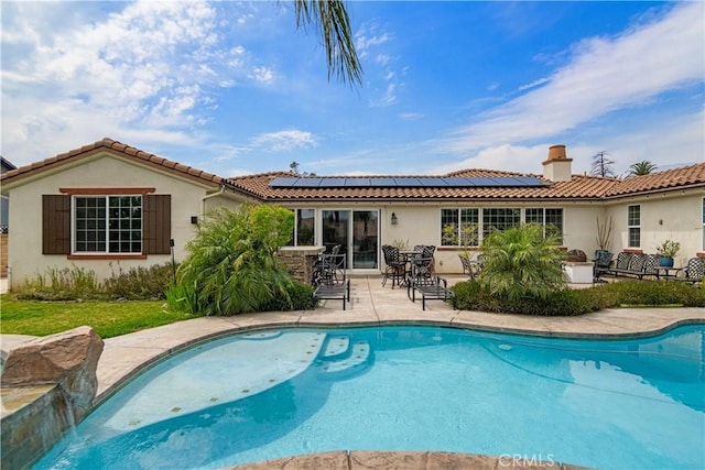 rear view of house with stucco siding, an outdoor pool, and a tiled roof