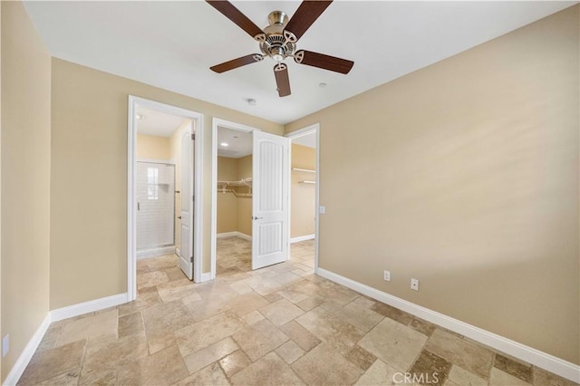 unfurnished bedroom featuring a ceiling fan, a closet, a walk in closet, stone tile flooring, and baseboards