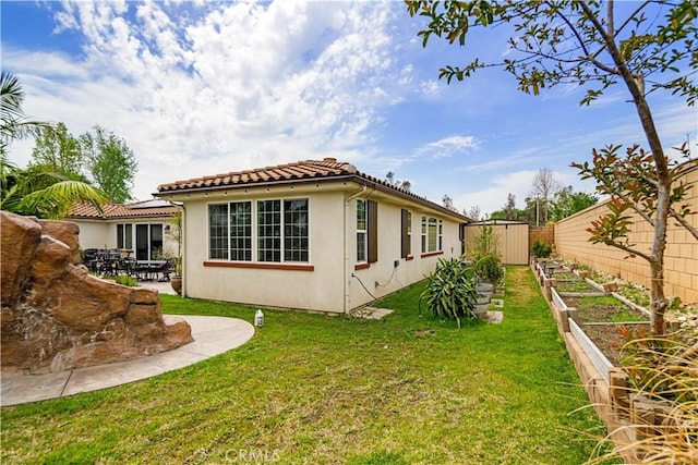 view of side of home featuring a tiled roof, fence, a lawn, a vegetable garden, and stucco siding