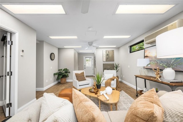 living area with ceiling fan, baseboards, wood finished floors, and a skylight