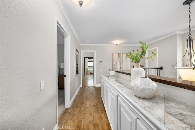 corridor with wood finished floors, crown molding, baseboards, and a textured wall