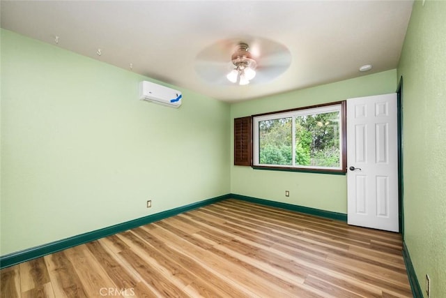 empty room with light wood finished floors, baseboards, a ceiling fan, and an AC wall unit
