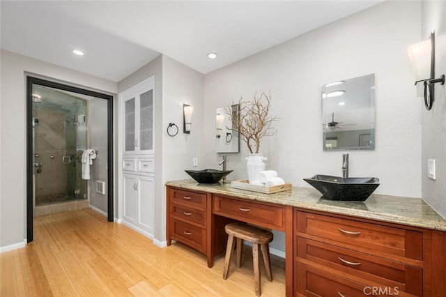 bathroom with double vanity, wood finished floors, a stall shower, and a sink