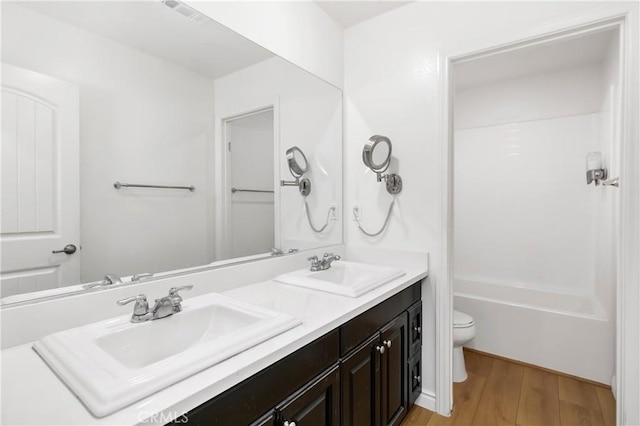 bathroom with double vanity, wood finished floors, toilet, and a sink