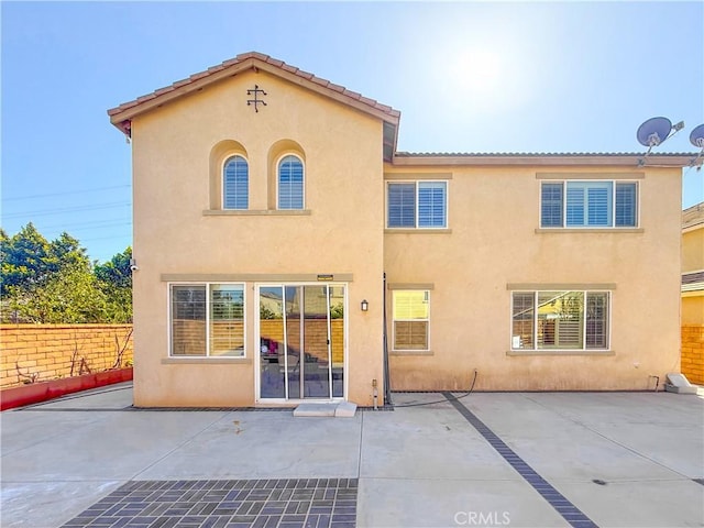 rear view of property featuring stucco siding, fence, and a patio