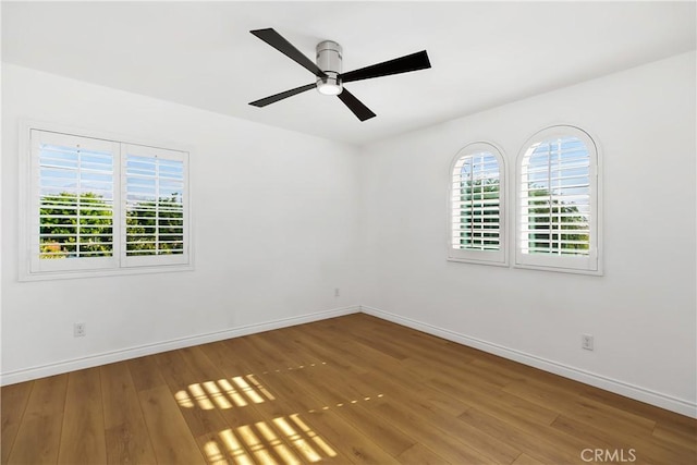 spare room with wood finished floors, a ceiling fan, and baseboards