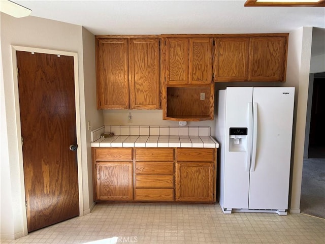 kitchen with brown cabinetry, white fridge with ice dispenser, and tile countertops
