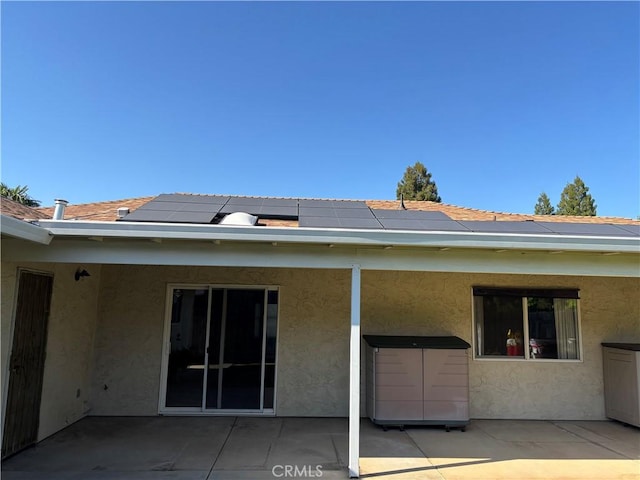 rear view of house with roof mounted solar panels, a patio area, and stucco siding