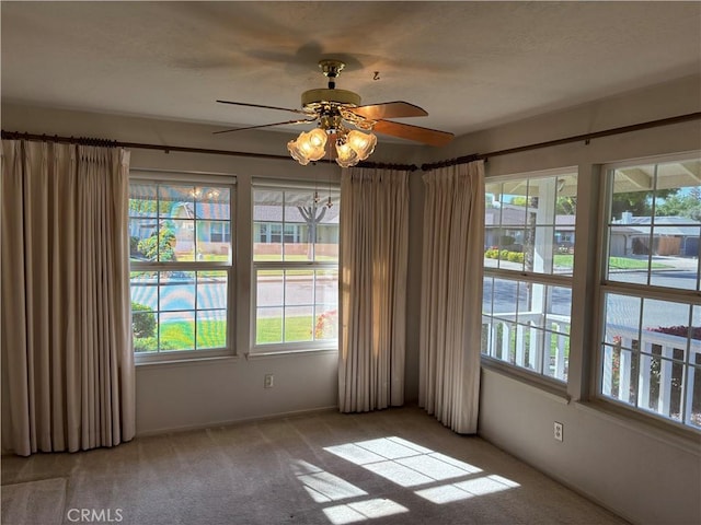 carpeted empty room with a wealth of natural light, a ceiling fan, and baseboards