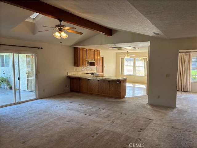 kitchen featuring a peninsula, vaulted ceiling with beams, light colored carpet, a ceiling fan, and brown cabinets