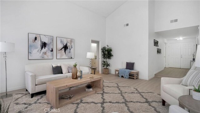 living area with visible vents, wood finished floors, high vaulted ceiling, and baseboards