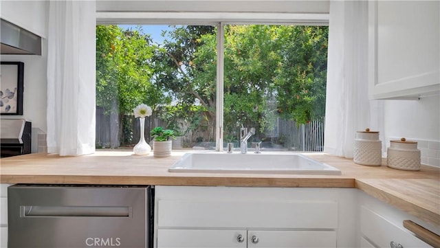 interior space with butcher block counters, white cabinetry, dishwasher, and a sink
