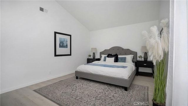 bedroom featuring baseboards, visible vents, wood finished floors, and vaulted ceiling