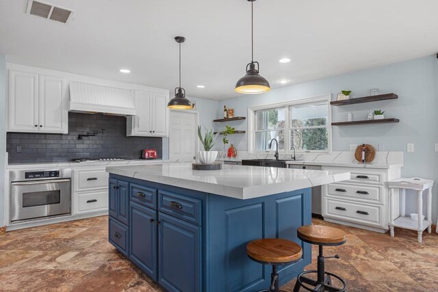 22053 Highland St, Wildomar, CA 92595 - kitchen with stainless steel appliances, open shelves, blue cabinets, premium range hood, and white cabinetry