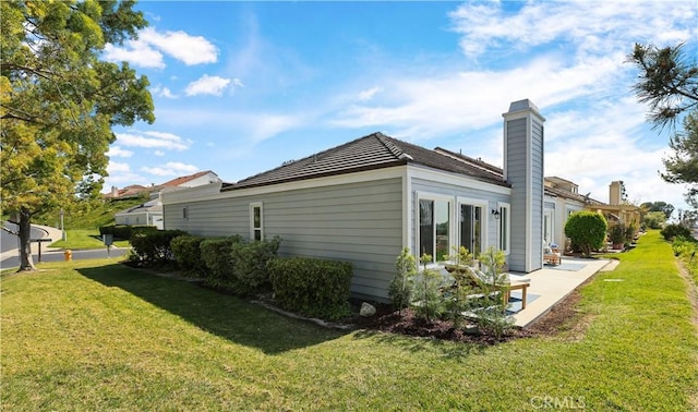 view of side of property featuring a patio, a chimney, and a yard
