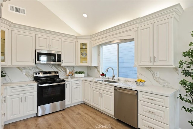 kitchen featuring lofted ceiling, a sink, visible vents, stainless steel appliances, and backsplash