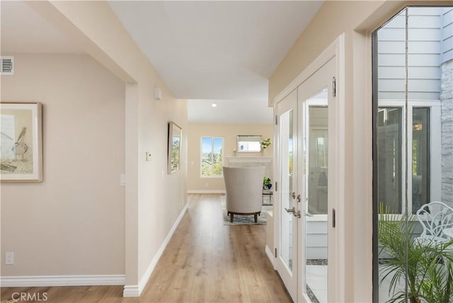 corridor with visible vents, baseboards, french doors, and light wood-style floors