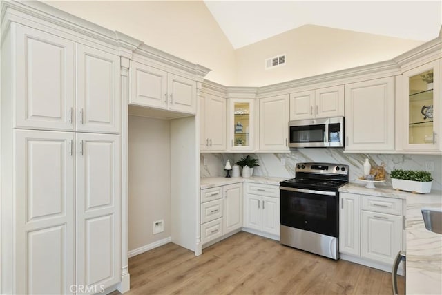 kitchen featuring glass insert cabinets, visible vents, stainless steel appliances, vaulted ceiling, and backsplash