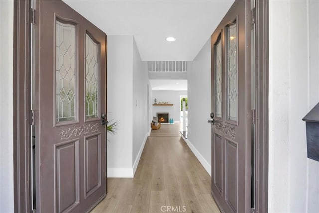 entrance foyer with light wood finished floors, baseboards, a warm lit fireplace, and recessed lighting