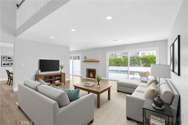 living room featuring recessed lighting, light wood finished floors, a fireplace with flush hearth, and baseboards