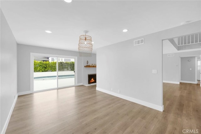 unfurnished living room featuring wood finished floors, a lit fireplace, baseboards, and recessed lighting