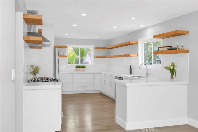 kitchen with open shelves, a sink, wall chimney exhaust hood, light wood-type flooring, and recessed lighting