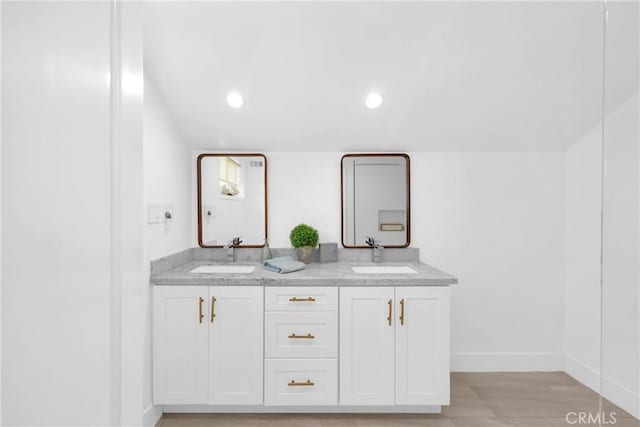 bathroom with baseboards, double vanity, recessed lighting, and wood finished floors