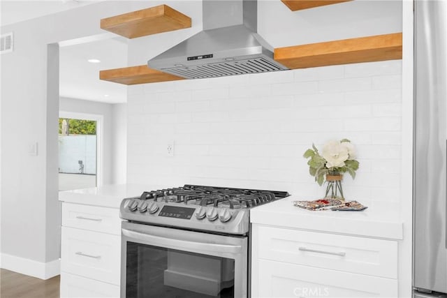 kitchen featuring gas range, wall chimney range hood, backsplash, light countertops, and white cabinets