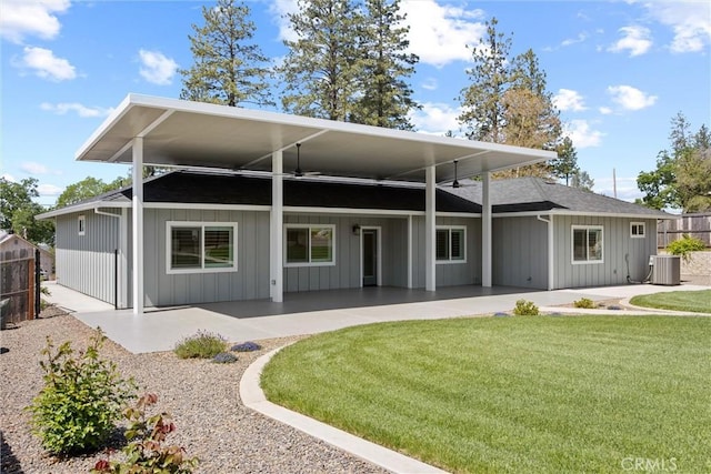 rear view of house with central AC unit, fence, a patio area, a lawn, and board and batten siding