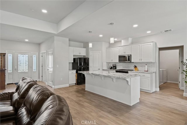 kitchen featuring decorative backsplash, open floor plan, stainless steel microwave, visible vents, and freestanding refrigerator