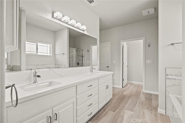 full bathroom with wood finished floors, a sink, a stall shower, double vanity, and visible vents