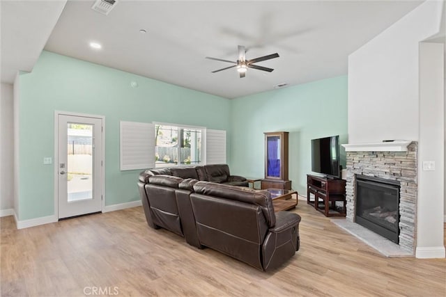 living room featuring a ceiling fan, visible vents, a fireplace, and light wood-style flooring
