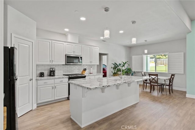 kitchen with white cabinets, light stone counters, stainless steel appliances, a sink, and tasteful backsplash