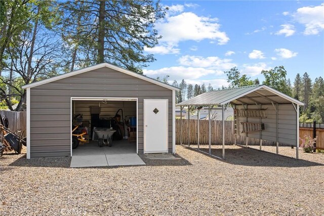 detached garage featuring fence and a carport