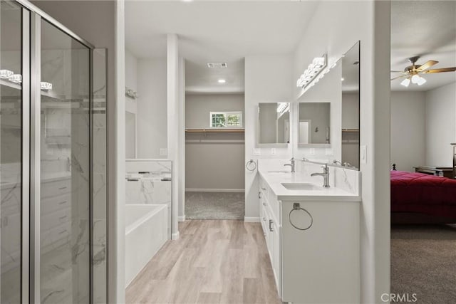 ensuite bathroom featuring wood finished floors, a stall shower, ceiling fan, and a sink