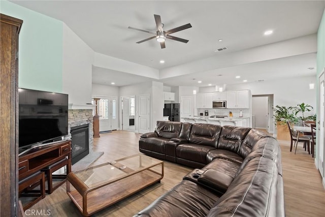 living area featuring light wood-type flooring, a stone fireplace, visible vents, and ceiling fan